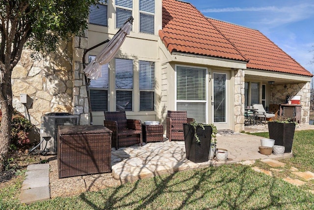 rear view of house with stone siding, central AC, a tile roof, and a patio area