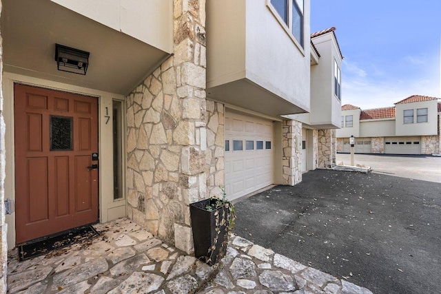 doorway to property featuring stucco siding, driveway, and stone siding