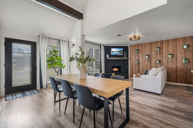 dining space featuring a warm lit fireplace, visible vents, wood finished floors, and beam ceiling