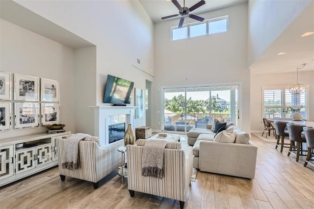 6914 Halesboro Dr, Austin, TX 78736 - living room featuring a glass covered fireplace, ceiling fan with notable chandelier, a high ceiling, and a wealth of natural light