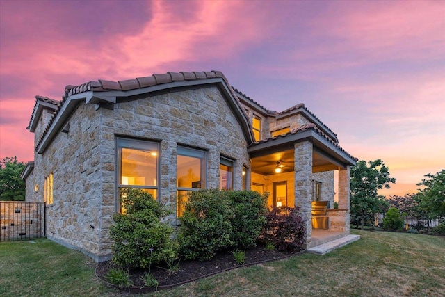 modern home with fence, a front yard, a tile roof, and stone siding