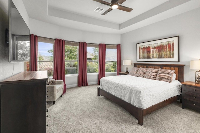 carpeted bedroom with ceiling fan, visible vents, and a raised ceiling