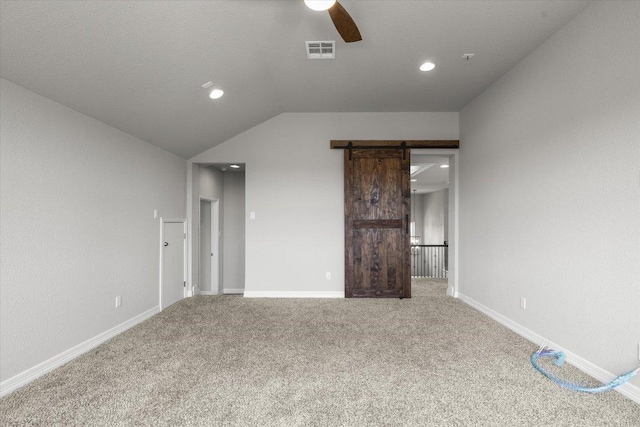 unfurnished bedroom featuring a ceiling fan, visible vents, vaulted ceiling, a barn door, and carpet flooring
