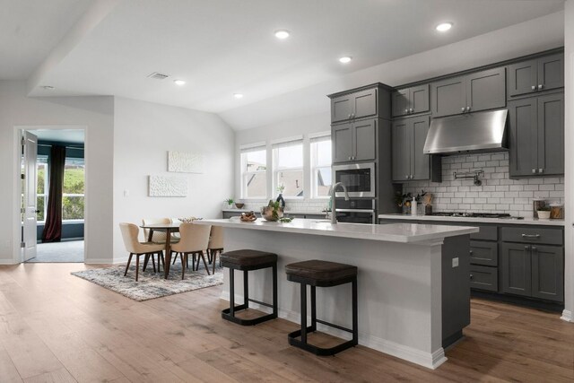 kitchen featuring dark wood-type flooring, gray cabinets, under cabinet range hood, and tasteful backsplash