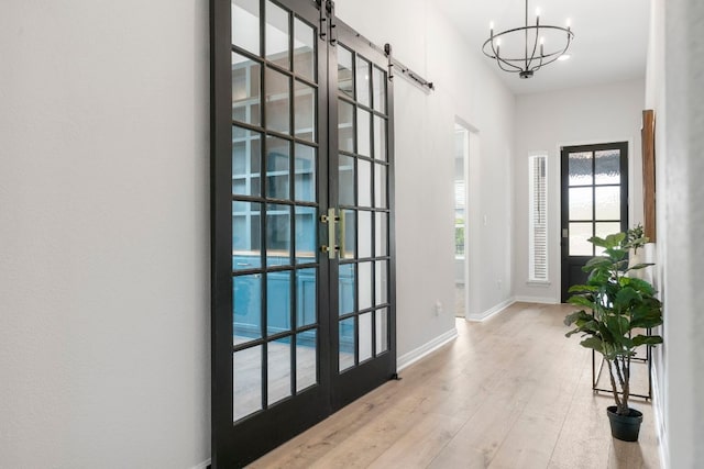 entryway with french doors, a barn door, baseboards, wood-type flooring, and a notable chandelier