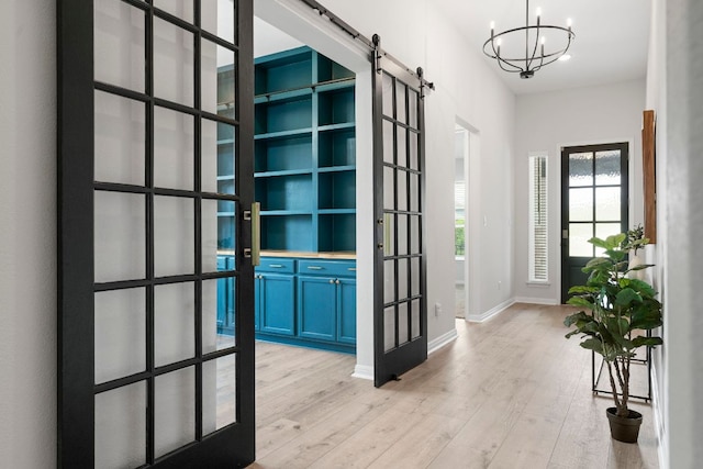 foyer entrance featuring baseboards, a barn door, french doors, light wood-style flooring, and a notable chandelier