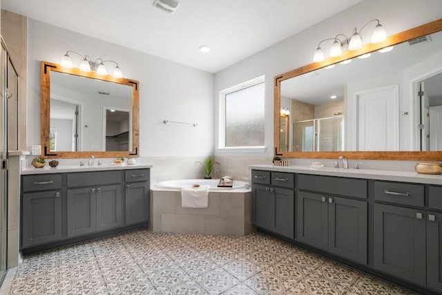 full bath with visible vents, a garden tub, two vanities, a sink, and a stall shower