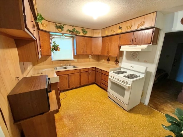 kitchen featuring brown cabinetry, a textured ceiling, a sink, white range with gas cooktop, and under cabinet range hood