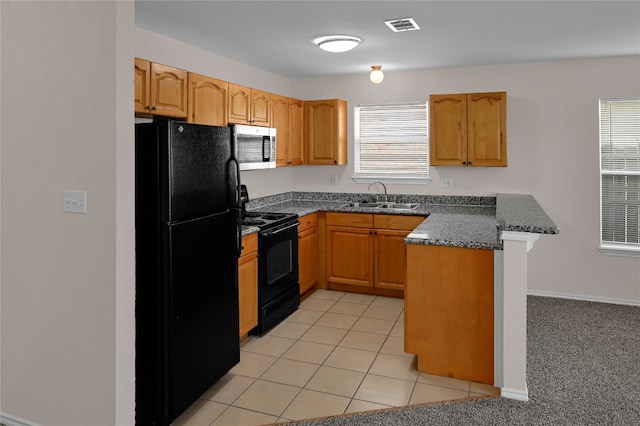 kitchen featuring visible vents, a peninsula, a kitchen breakfast bar, a sink, and black appliances