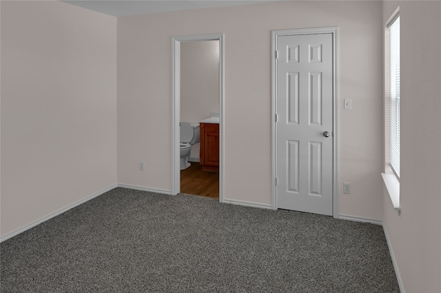 unfurnished bedroom with baseboards, ensuite bathroom, and carpet