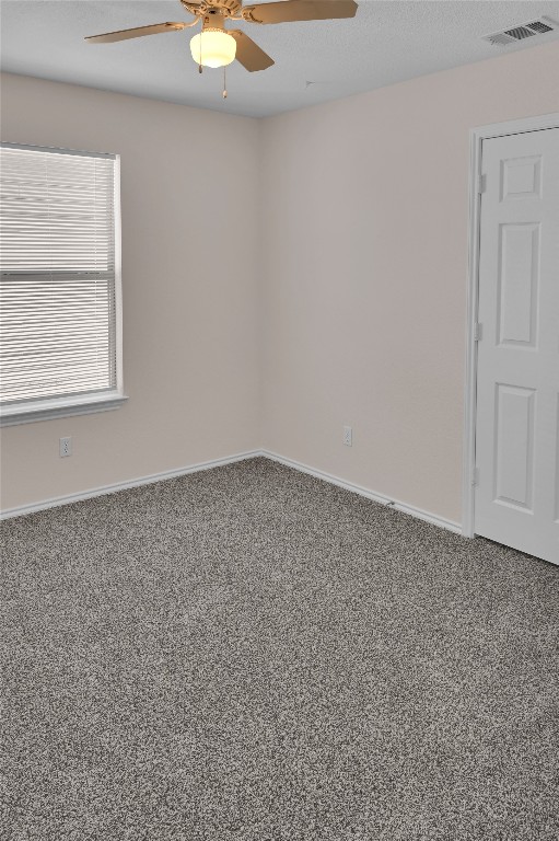 carpeted empty room featuring ceiling fan, visible vents, and baseboards