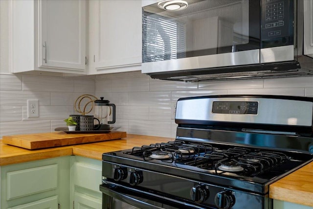 kitchen with white cabinets, gas stove, butcher block countertops, stainless steel microwave, and tasteful backsplash