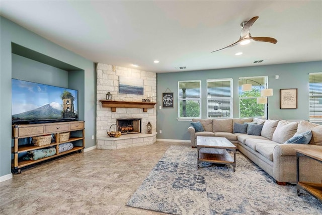 living area with a stone fireplace, a ceiling fan, baseboards, and visible vents