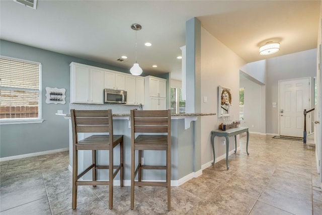 kitchen featuring white cabinets, light stone countertops, stainless steel microwave, decorative light fixtures, and a kitchen bar