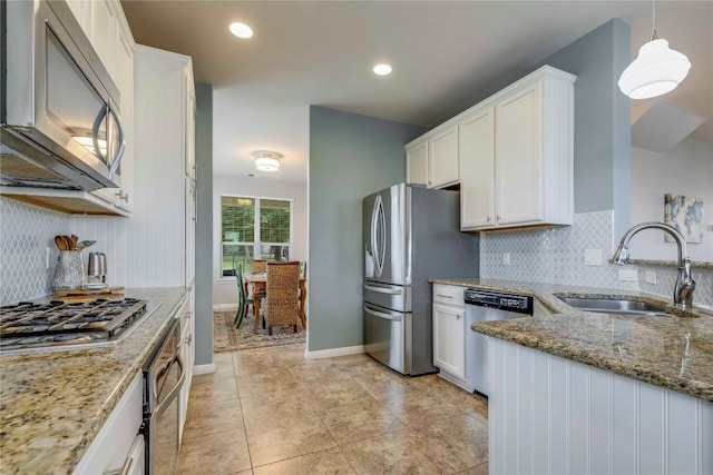 kitchen with white cabinets, stainless steel appliances, light stone countertops, and a sink