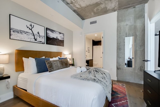 bedroom with connected bathroom, visible vents, and wood finished floors