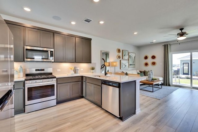 kitchen with light countertops, stainless steel appliances, a peninsula, light wood-type flooring, and visible vents