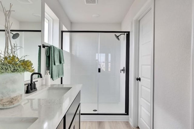 full bath featuring double vanity, visible vents, a shower stall, wood finished floors, and a sink