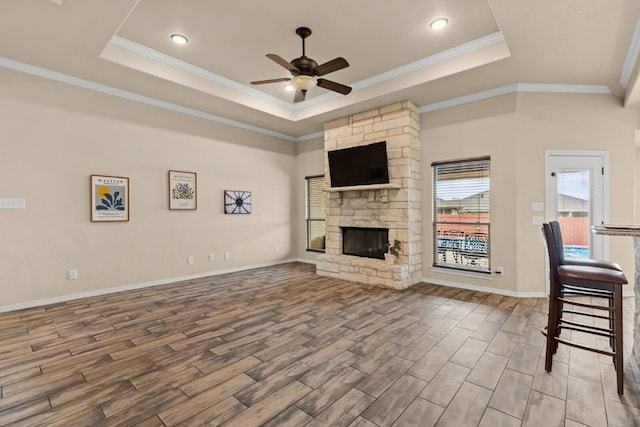 unfurnished living room with a raised ceiling, ceiling fan, wood finished floors, and a fireplace