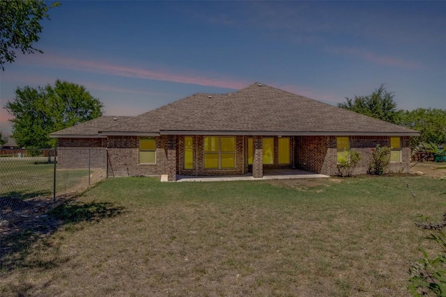 rear view of property featuring brick siding, roof with shingles, fence, and a yard