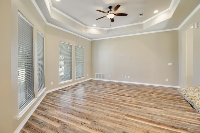 empty room featuring ceiling fan, visible vents, a raised ceiling, and light wood-type flooring