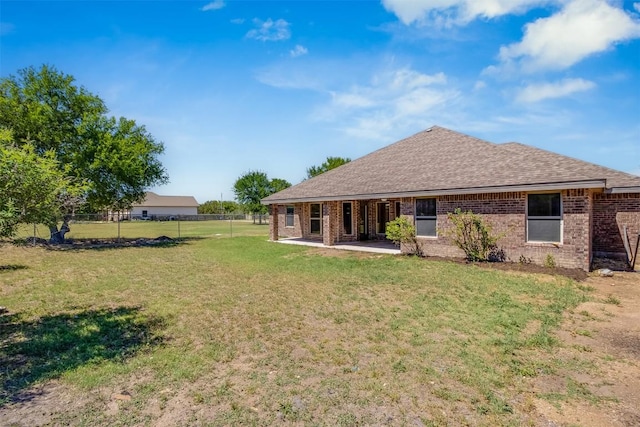 rear view of property featuring fence, a patio, brick siding, a shingled roof, and a yard