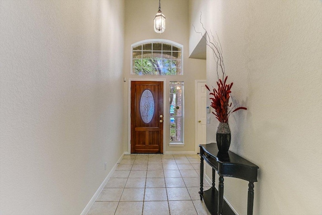 foyer entrance with baseboards, light tile patterned flooring, and a towering ceiling