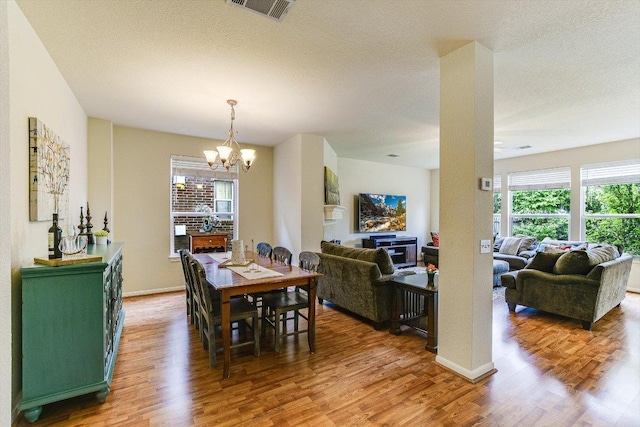 dining room featuring a notable chandelier, a textured ceiling, baseboards, wood finished floors, and visible vents