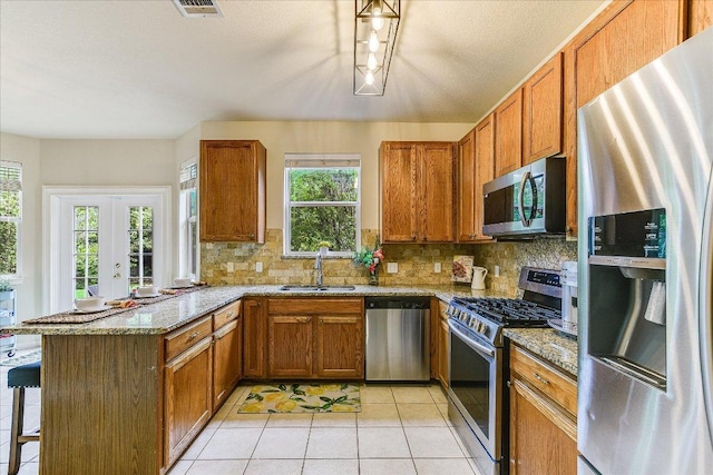 kitchen with a sink, appliances with stainless steel finishes, brown cabinets, and a peninsula