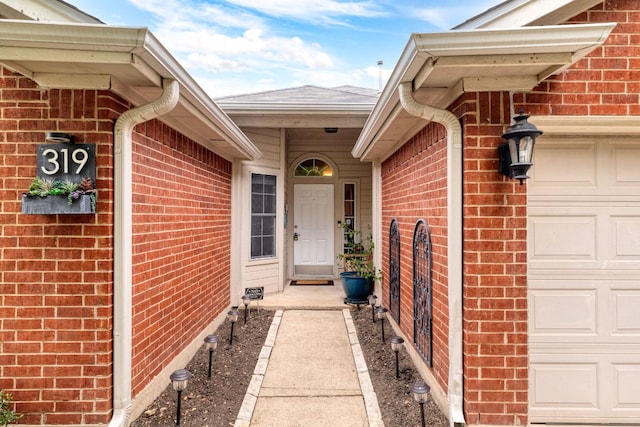 entrance to property featuring a garage, roof with shingles, and brick siding
