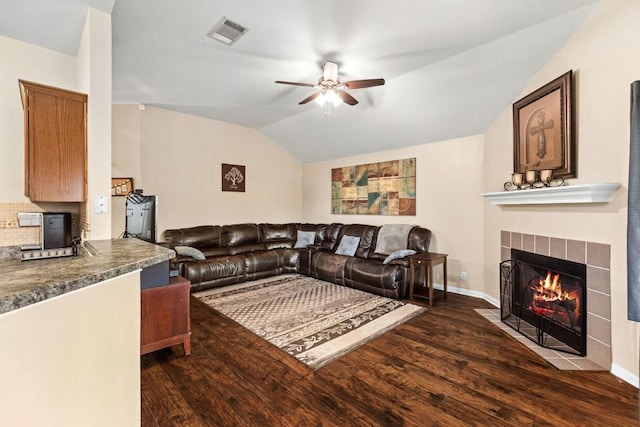 living area featuring visible vents, dark wood-style flooring, ceiling fan, a tile fireplace, and vaulted ceiling