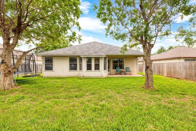 back of house featuring a patio, a fenced backyard, a trampoline, and a yard