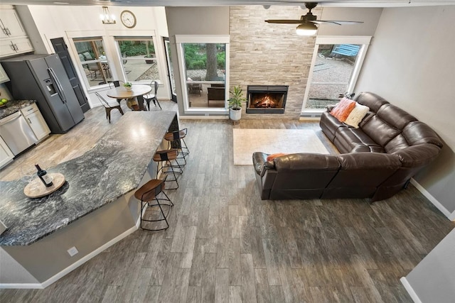 living area with baseboards, a ceiling fan, a large fireplace, and wood finished floors