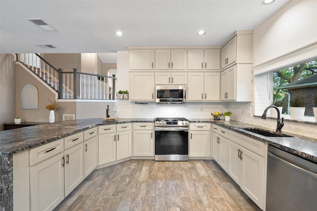 kitchen with visible vents, appliances with stainless steel finishes, a sink, a peninsula, and light wood-style floors