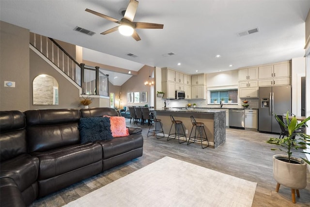 living room featuring visible vents, lofted ceiling, light wood-style flooring, and ceiling fan with notable chandelier