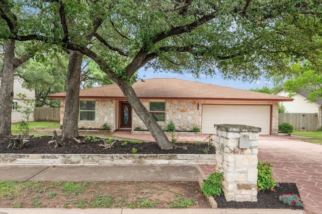 ranch-style house featuring an attached garage, fence, driveway, and stone siding