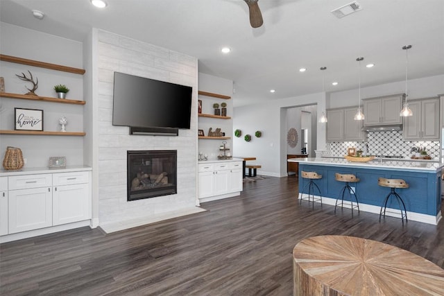 living room featuring dark wood-style flooring, ceiling fan, a fireplace, recessed lighting, and visible vents