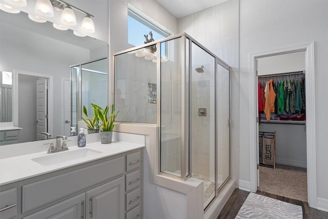 full bath featuring vanity, a shower stall, wood finished floors, and a walk in closet
