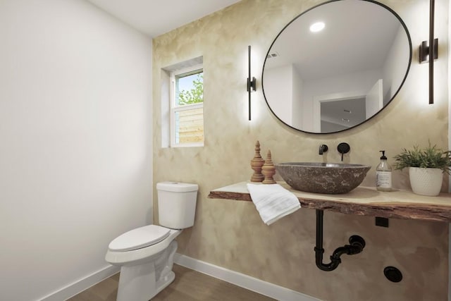 half bathroom with baseboards, a sink, wood finished floors, and toilet