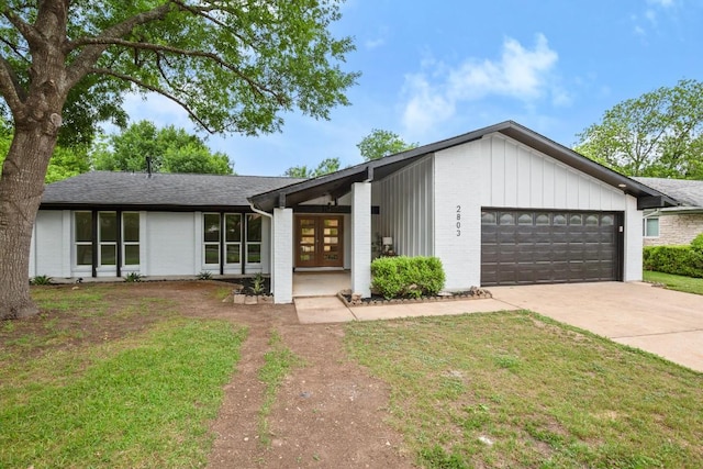 view of front of house featuring french doors, a front yard, brick siding, concrete driveway, and an attached garage