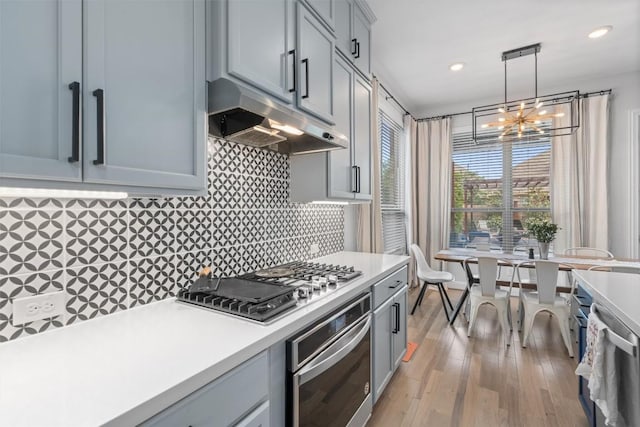 kitchen with an inviting chandelier, decorative backsplash, light countertops, under cabinet range hood, and stainless steel appliances