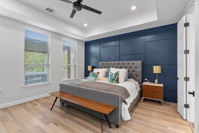 bedroom featuring visible vents, baseboards, recessed lighting, a tray ceiling, and light wood-style flooring
