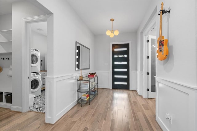 foyer entrance with stacked washer and clothes dryer, light wood-style flooring, and wainscoting