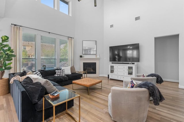 living room with baseboards, visible vents, light wood-style flooring, and a towering ceiling