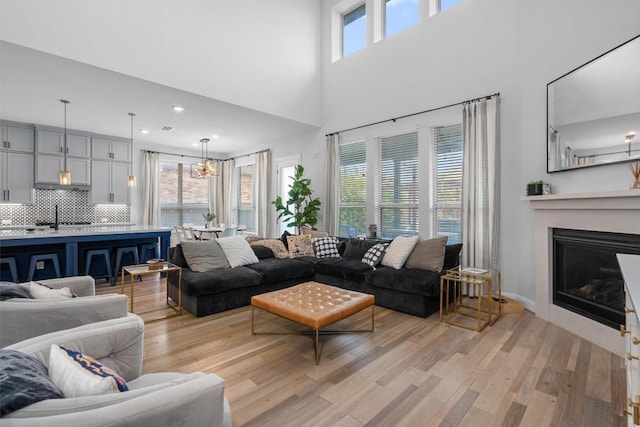 living room with recessed lighting, a high ceiling, a glass covered fireplace, and light wood-type flooring