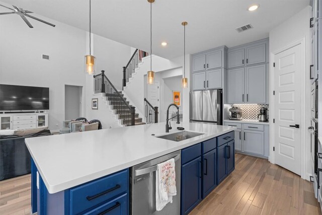 20620 Lukes Cv, Pflugerville, TX 78660 - kitchen featuring stainless steel appliances, a sink, open floor plan, light wood-type flooring, and blue cabinets