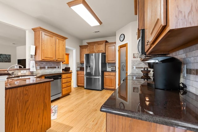 kitchen with a sink, decorative backsplash, light wood finished floors, and stainless steel appliances