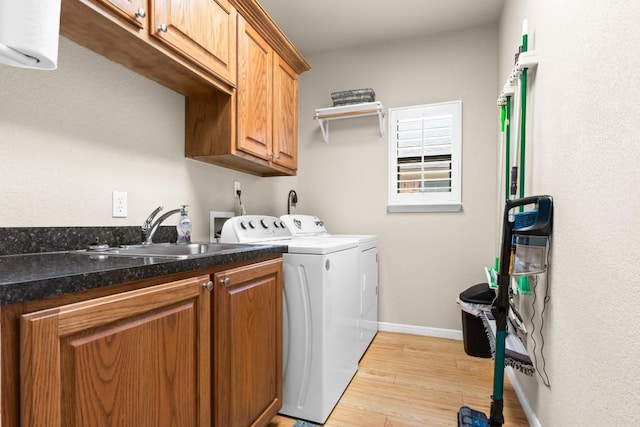 clothes washing area featuring independent washer and dryer, light wood-type flooring, cabinet space, a sink, and baseboards
