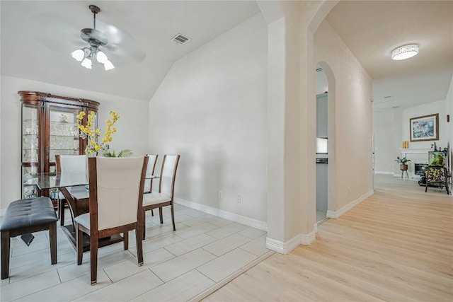 dining room with visible vents, a ceiling fan, lofted ceiling, arched walkways, and light wood-style flooring