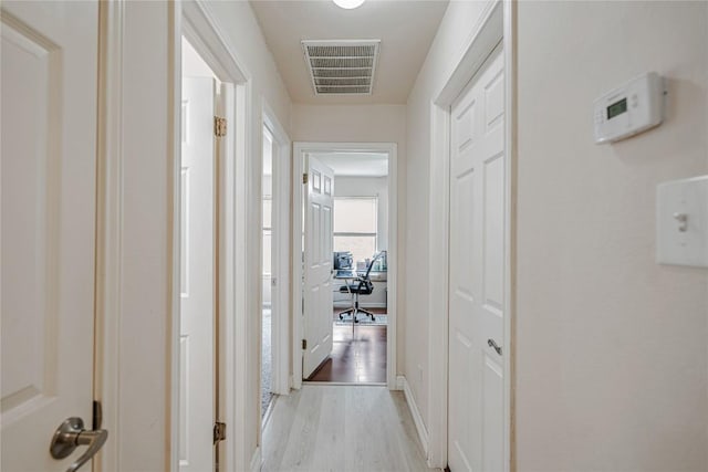 corridor featuring light wood-style floors, baseboards, and visible vents
